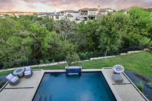 pool at dusk featuring pool water feature and a lawn