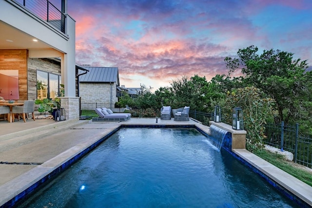 pool at dusk with pool water feature and a patio