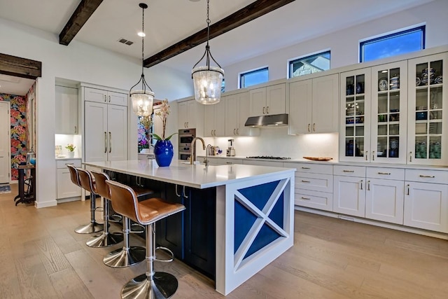 kitchen with white cabinets, a breakfast bar, decorative light fixtures, beamed ceiling, and an island with sink