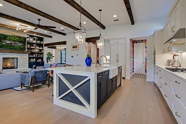 kitchen featuring sink, a center island with sink, white cabinets, a stone fireplace, and hanging light fixtures