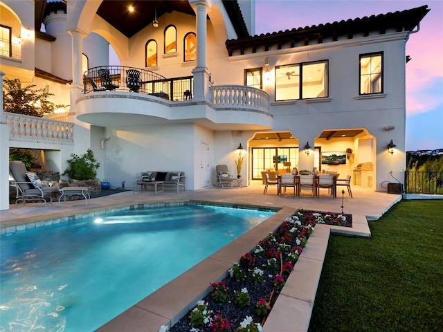 back house at dusk featuring a patio and a balcony