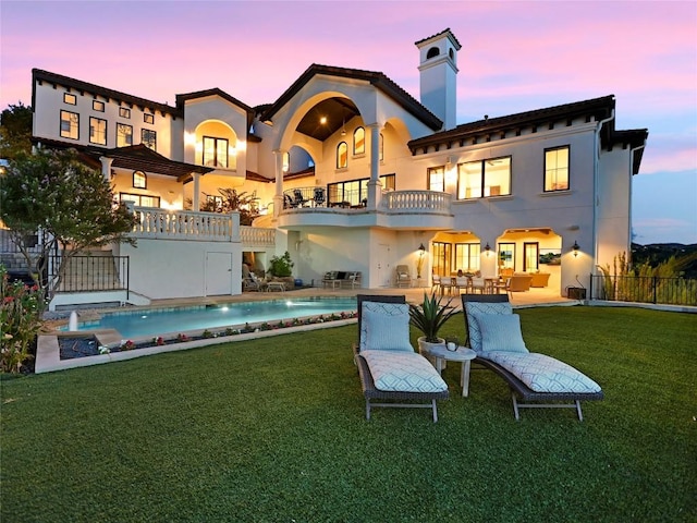 back house at dusk featuring a yard, a patio, and a balcony