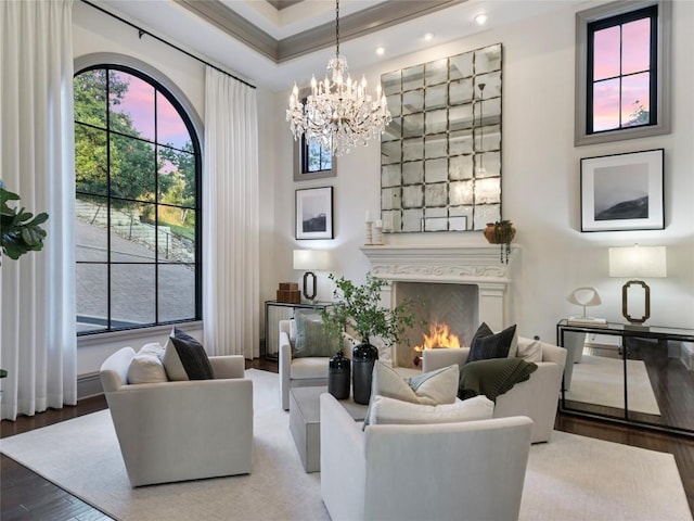 living room with ornamental molding, a large fireplace, a raised ceiling, hardwood / wood-style flooring, and a notable chandelier