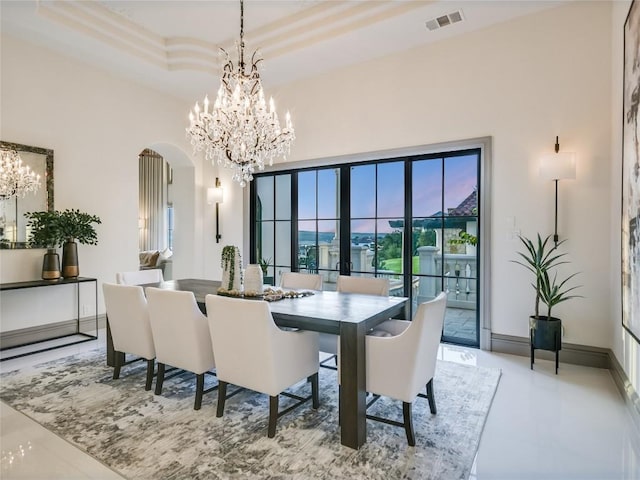 dining space with a towering ceiling, a tray ceiling, and a chandelier