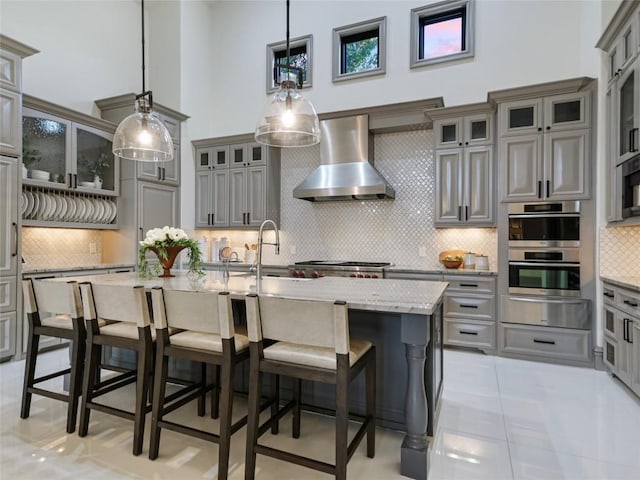 kitchen featuring pendant lighting, an island with sink, appliances with stainless steel finishes, and wall chimney range hood