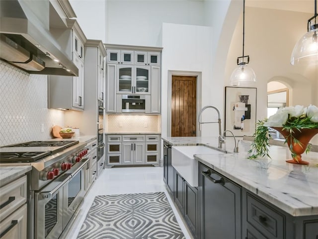 kitchen featuring wall chimney range hood, hanging light fixtures, gray cabinets, appliances with stainless steel finishes, and tasteful backsplash