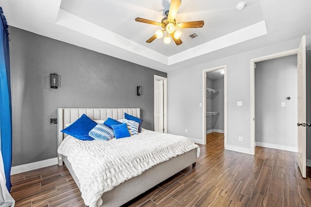 bedroom with a walk in closet, a tray ceiling, and ceiling fan