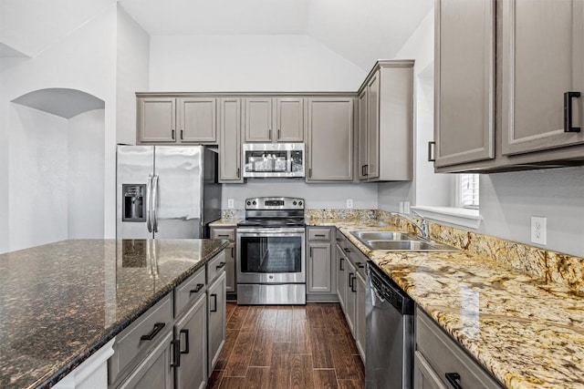 kitchen with stainless steel appliances, dark wood-type flooring, sink, dark stone countertops, and lofted ceiling