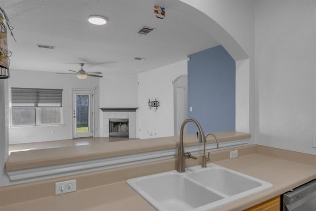 kitchen with a tile fireplace, ceiling fan, dishwashing machine, and sink