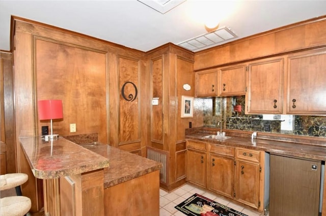 kitchen featuring kitchen peninsula, a kitchen breakfast bar, decorative backsplash, sink, and light tile patterned floors