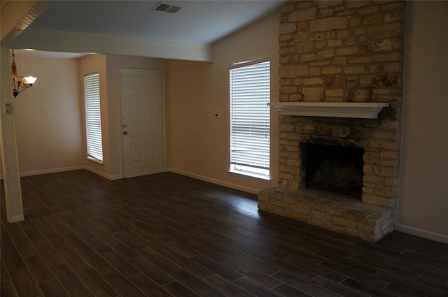 unfurnished living room featuring a stone fireplace, dark wood-type flooring, a healthy amount of sunlight, and a notable chandelier