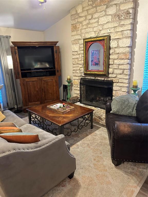 living area featuring light wood-style flooring, lofted ceiling, and a stone fireplace