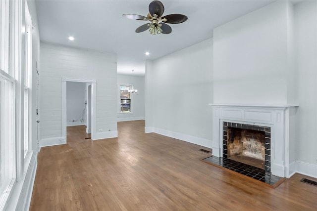 unfurnished living room featuring hardwood / wood-style floors, ceiling fan with notable chandelier, and a tiled fireplace