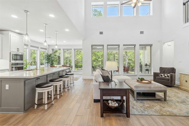 living room with ceiling fan, a healthy amount of sunlight, a high ceiling, and light hardwood / wood-style flooring