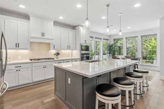 kitchen with stainless steel appliances, a kitchen island with sink, white cabinets, and hanging light fixtures