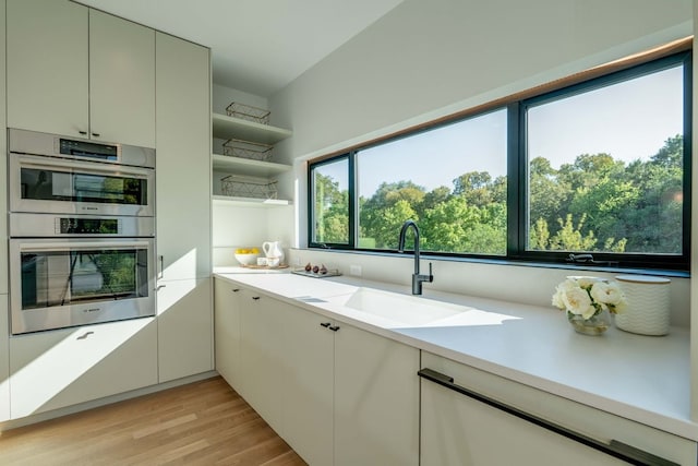 kitchen featuring light wood-type flooring, stainless steel double oven, plenty of natural light, and sink