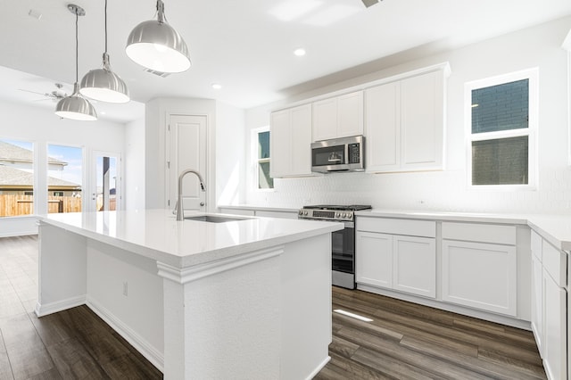 kitchen with dark wood finished floors, a center island with sink, pendant lighting, appliances with stainless steel finishes, and a sink