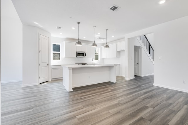 kitchen with visible vents, light wood-style flooring, stainless steel microwave, white cabinets, and light countertops