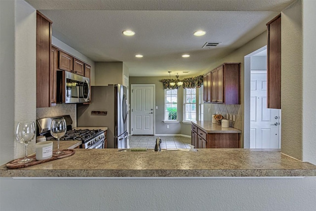 kitchen with a notable chandelier, kitchen peninsula, a textured ceiling, decorative backsplash, and appliances with stainless steel finishes