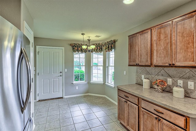 kitchen with stainless steel refrigerator, a notable chandelier, pendant lighting, decorative backsplash, and light tile patterned floors