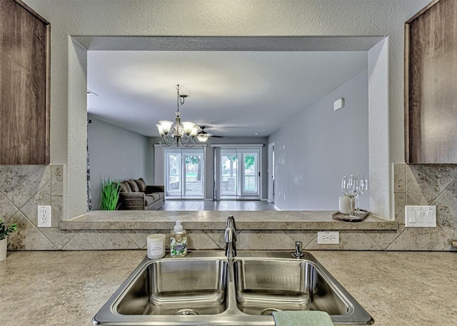 kitchen with backsplash, ceiling fan with notable chandelier, and sink