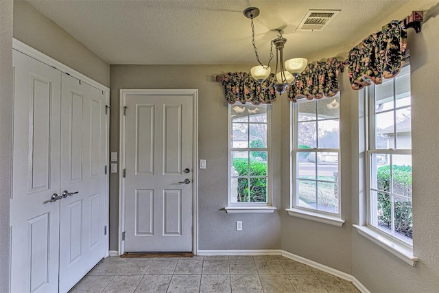 doorway with light tile patterned floors, a textured ceiling, and a notable chandelier