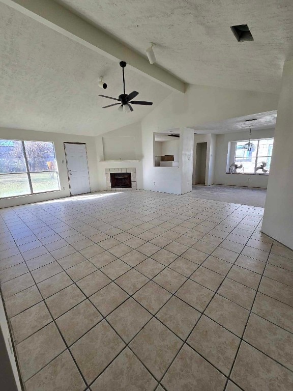 unfurnished living room with vaulted ceiling with beams, a textured ceiling, a tiled fireplace, light tile patterned floors, and ceiling fan with notable chandelier