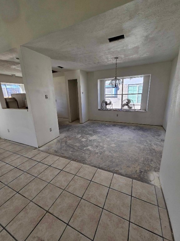 unfurnished dining area with light tile patterned flooring, a chandelier, and a textured ceiling