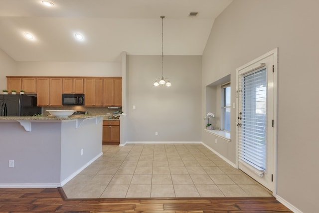 kitchen featuring light hardwood / wood-style flooring, a notable chandelier, pendant lighting, a breakfast bar area, and black appliances