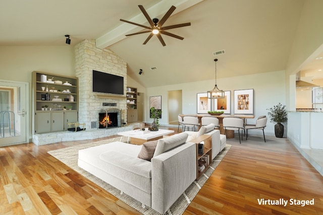 living room with ceiling fan with notable chandelier, beam ceiling, light hardwood / wood-style flooring, high vaulted ceiling, and a stone fireplace