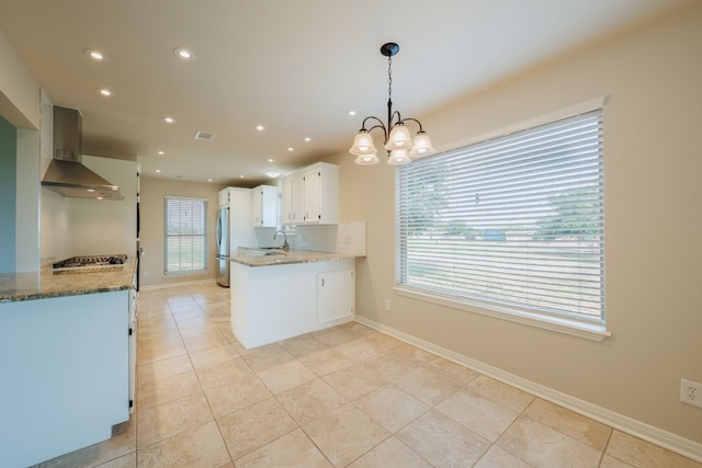 kitchen featuring appliances with stainless steel finishes, wall chimney range hood, white cabinetry, hanging light fixtures, and light tile patterned flooring