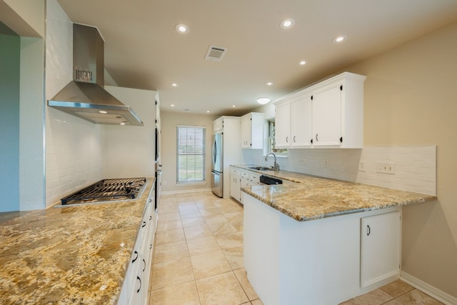 kitchen featuring wall chimney exhaust hood, appliances with stainless steel finishes, tasteful backsplash, light stone counters, and white cabinetry