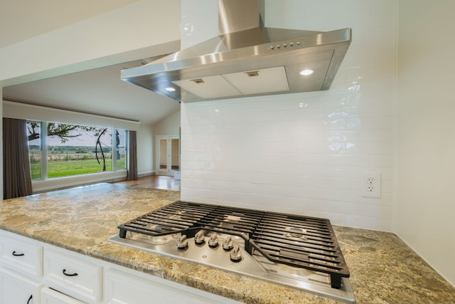 kitchen with stainless steel gas stovetop, lofted ceiling, white cabinets, island range hood, and light stone counters