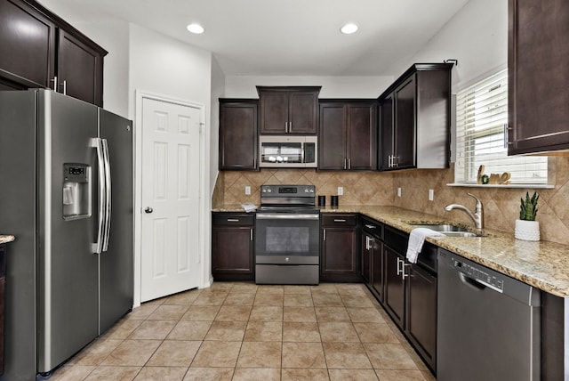 kitchen featuring appliances with stainless steel finishes, backsplash, light stone counters, light tile patterned floors, and dark brown cabinets