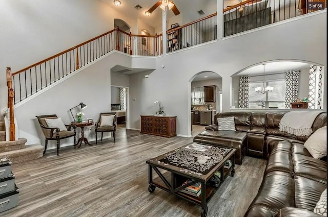 living room with wood-type flooring, ceiling fan with notable chandelier, and a towering ceiling