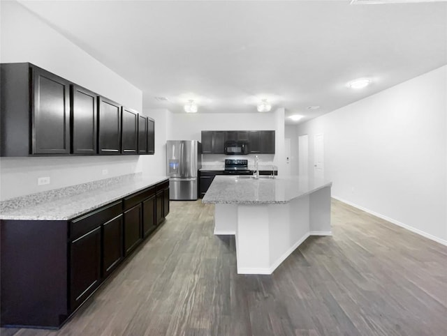 kitchen featuring light stone countertops, sink, black appliances, light hardwood / wood-style flooring, and an island with sink