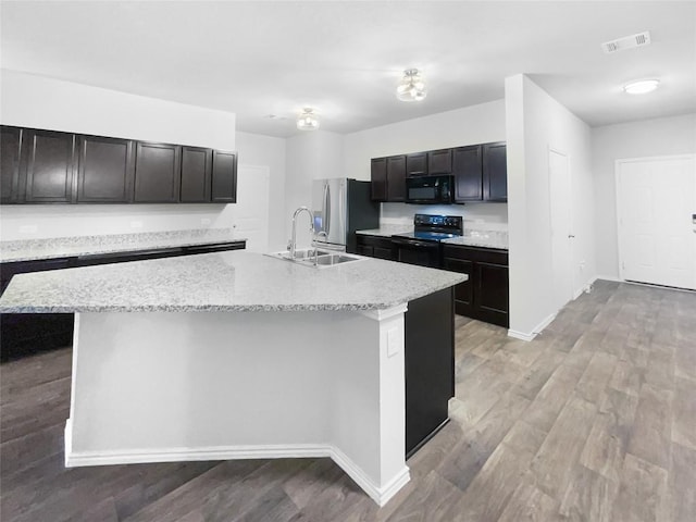 kitchen with light stone countertops, sink, a kitchen island with sink, black appliances, and light wood-type flooring