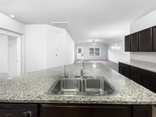 kitchen with light stone countertops, sink, dishwasher, a kitchen island with sink, and ceiling fan with notable chandelier