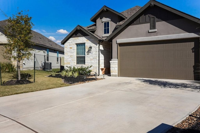 view of front of house featuring an attached garage, fence, stone siding, driveway, and stucco siding