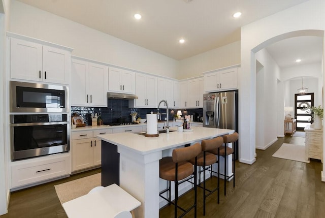 kitchen featuring appliances with stainless steel finishes, a kitchen island with sink, white cabinetry, backsplash, and a kitchen bar