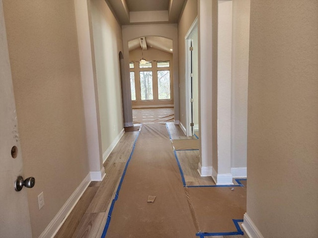 hall featuring arched walkways, wood finished floors, and baseboards