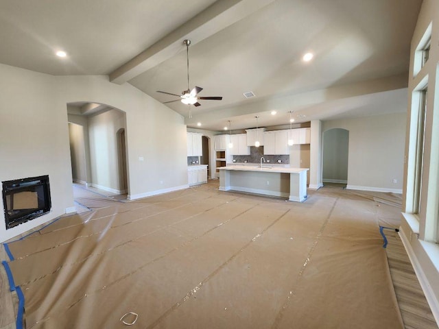 unfurnished living room featuring arched walkways, a sink, lofted ceiling with beams, and baseboards