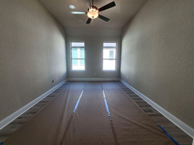 spare room with wood finished floors, a textured wall, baseboards, and ceiling fan