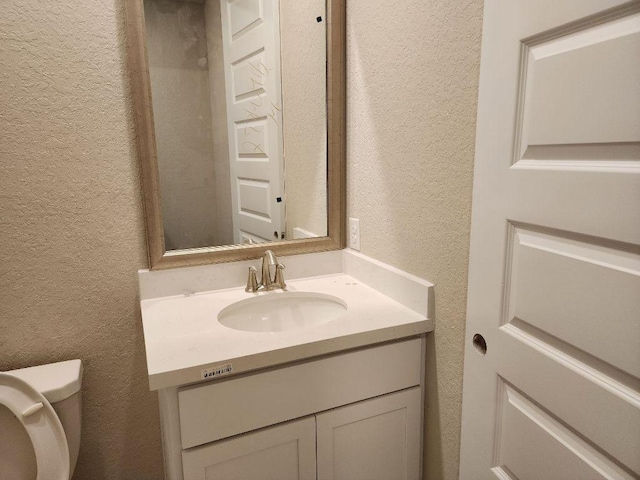 half bath featuring toilet, vanity, and a textured wall