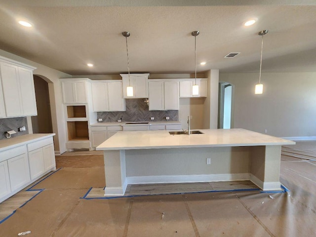 kitchen with visible vents, arched walkways, decorative backsplash, an island with sink, and a sink