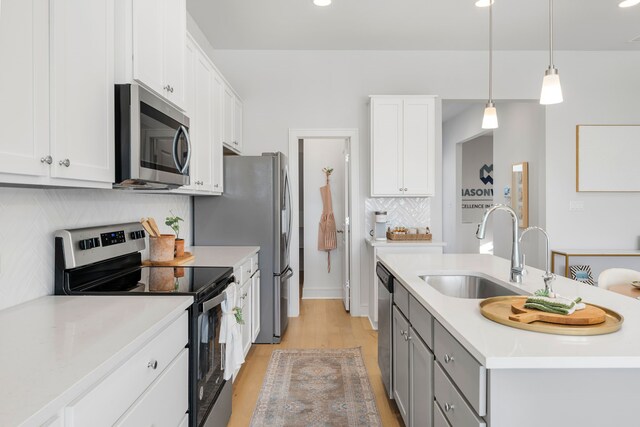 kitchen featuring appliances with stainless steel finishes, sink, decorative light fixtures, white cabinetry, and an island with sink