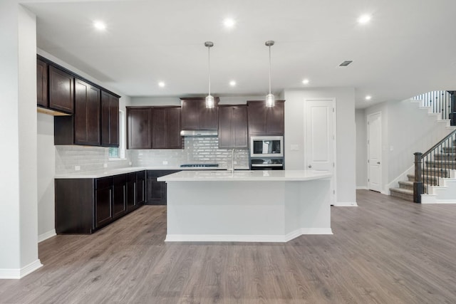 409 Raleigh Dr, Georgetown, TX 78633 - kitchen featuring stainless steel microwave, wall oven, under cabinet range hood, tasteful backsplash, and light wood finished floors