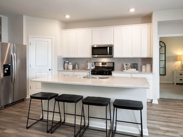 kitchen with white cabinets, stainless steel appliances, a kitchen island with sink, and sink