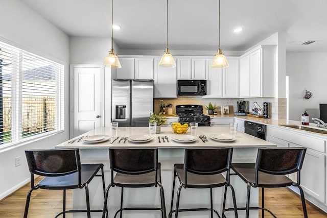 kitchen featuring a center island, decorative light fixtures, decorative backsplash, a breakfast bar, and black appliances