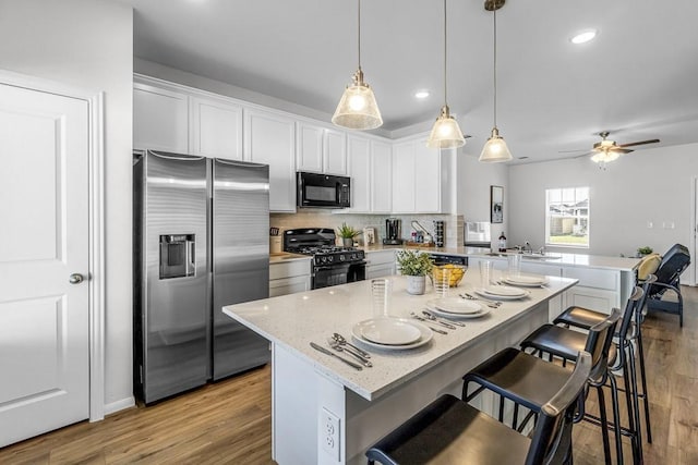 kitchen with a kitchen bar, a center island, white cabinetry, and black appliances